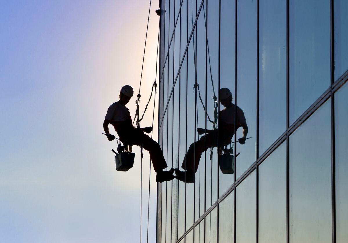 Facility management rope-access technician servicing the glass facade of a commercial tower at dusk